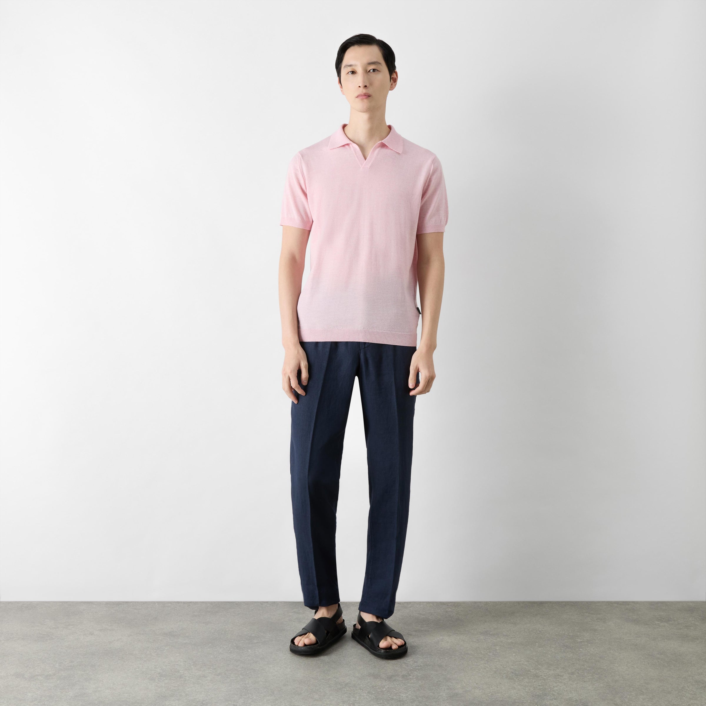 Man wearing a pink polo shirt and navy pants standing against a plain background